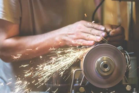 Man sharpens a metal blade on a machine. Man manufacturing in his workshop. Stock Photos