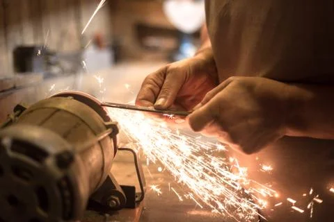 Man sharpens a metal blade on a machine. Man manufacturing in his workshop. Stock Photos