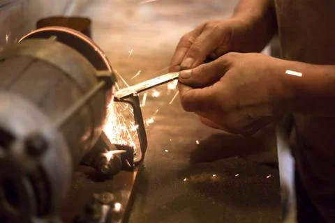 Man sharpens a metal blade on a machine. Man manufacturing in his workshop. Stock Photos