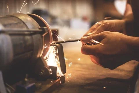 Man sharpens a metal blade on a machine. Man manufacturing in his workshop. Stock Photos
