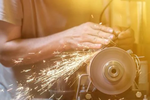 Man sharpens a metal blade on a machine. Man manufacturing in his workshop. Stock Photos