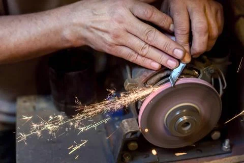Man sharpens a metal blade on a machine. Man manufacturing in his workshop. Stock Photos
