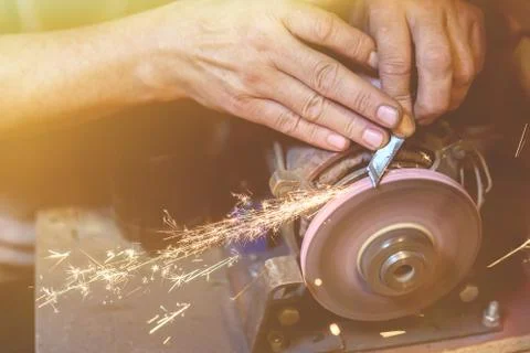 Man sharpens a metal blade on a machine. Man manufacturing in his workshop. Stock Photos