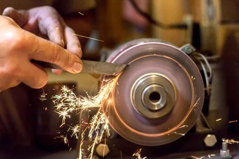 Man sharpens a metal blade on a machine. Man manufacturing in his workshop. Stock Photos
