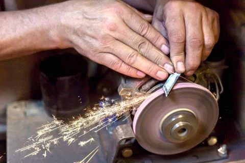 Man sharpens a metal blade on a machine. Man manufacturing in his workshop. Stock Photos