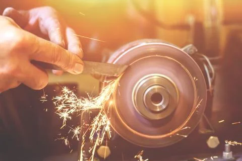 Man sharpens a metal blade on a machine. Man manufacturing in his workshop. Stock Photos