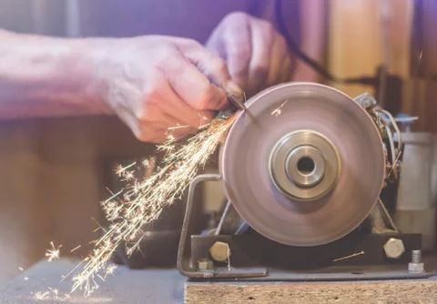 Man sharpens a metal blade on a machine. Man manufacturing in his workshop. Stock Photos
