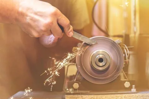Man sharpens a metal blade on a machine. Man manufacturing in his workshop. Stock Photos