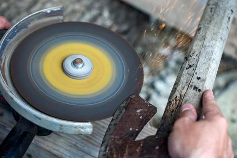 A man sharpens an old ax on a machine with sparks Stock Photos