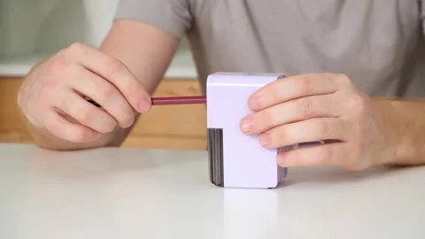 A man sharpens a pencil on desktop rotating pencil sharpener. Stock Footage 242298736