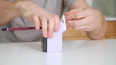 A man sharpens a pencil on desktop rotating pencil sharpener. Stock Footage 242444430
