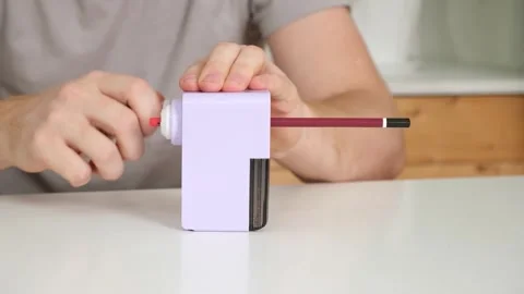A man sharpens a pencil on desktop rotating pencil sharpener. Stock Footage 242444444