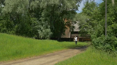 Man Sharpens the Scythe Rural Landscape Wooden Cottages in Park of Old Polish Stock Footage 63745111