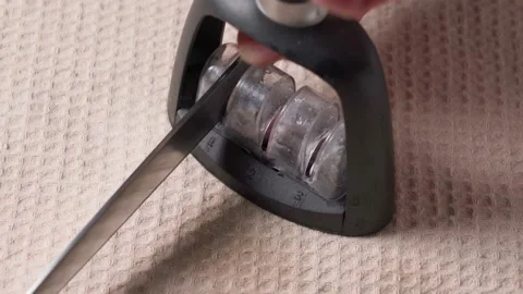 A man sharply sharpens knives on a sharpener on a table 4K Stock Footage 165751980