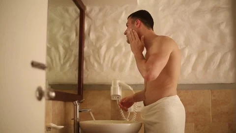Man shaves in front of the mirror in his bungalow bathroom on tropical island Stock Footage 78651276