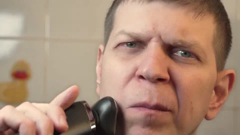 Man shaves his beard an electric razor in bathroom. Morning routine. Stock Footage 147997280
