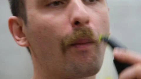 A man shaves his beard with an electric razor. The guy shaves off his big beard Stock Footage 232632989