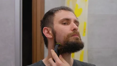 The man shaves his big beard. The guy shaves off his big beard. Young guy shaves Stock Footage 230504357