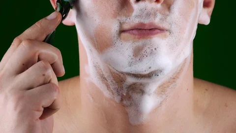 A man shaves his face with a machine on a green background.Close-up. Stock-Footage 127446273