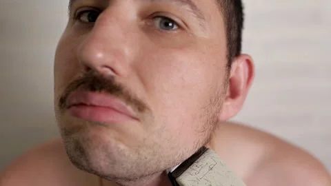 A man shaves a large beard with an electric razor. close-up portrait of a person 스톡 동영상 113210672