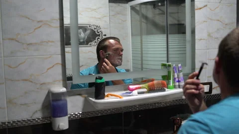 Man shaves with a razor in front of a mirror in the bathroom Stock Footage 101503657