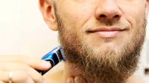 Man shaving beard using an electric razor. Man trimming beard at home. Видео 111297581