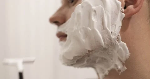Man is shaving on cheek with foam using disposable razor, closeup, side view. Stock Footage 137437919