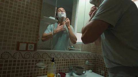 Man Shaving Face in Bathroom Mirror During Morning Routine Stock Footage 332068455