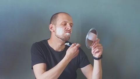 Man is shaving his beard with a small mirror in his hands Video stock 108056747