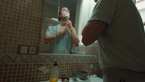 Man Shaving His Face with a Razor and Foam in the Bathroom Mirror Stock Footage 332068468