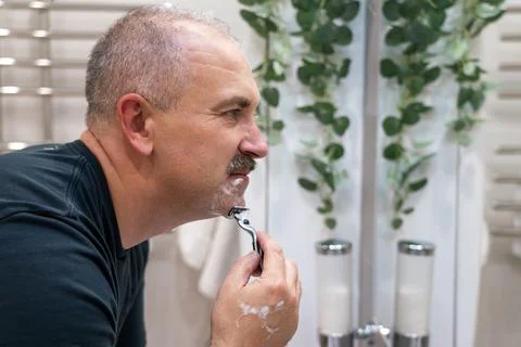 Man shaving with razor using foam in bathroom in the morning Stock Photos