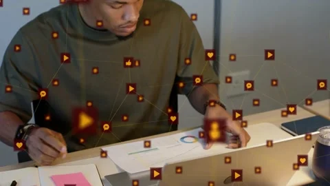 Man shifting from notes to laptop, reacting to overlay icons while comparing Stock Footage 332405508
