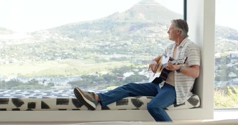 Man is shifting weight and centering guitar for playing and singing on window Stock Footage 338435981