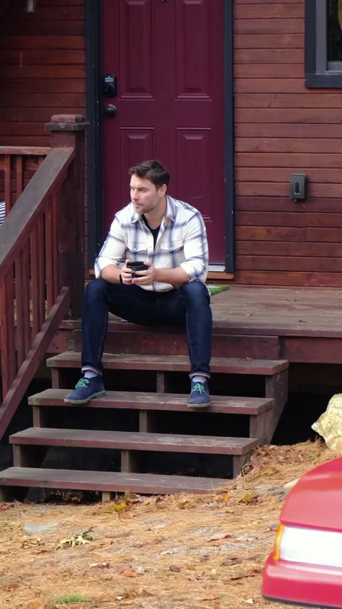 A man in a shirt drinking hot tea from a mug in the morning at the shallet house Stock Footage 295006114