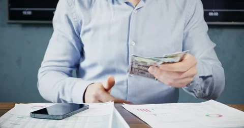 A man in a shirt sits at a table with papers and counts money Stock Footage 248726058