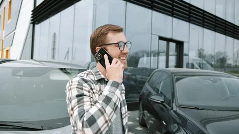 Man in shirt talks on his mobile phone outdoor and smiles near the car at salon Video stock 241417574