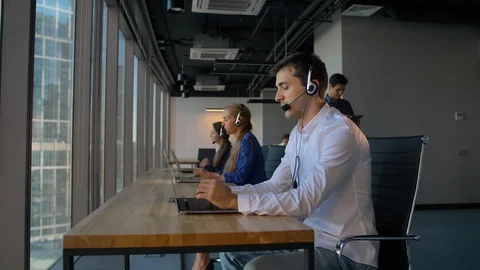 Man in shirt using a headset with laptop while working in call center office Vidéo 102533949