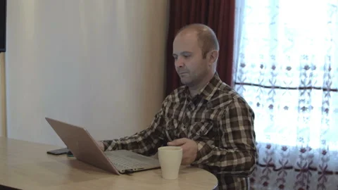 A man in a shirt works at the computer. Drinking hot morning coffee. HD Vídeo Stock 96114798