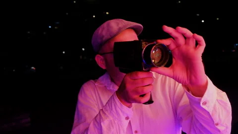 Man shooting and filming with a retro video camera by the neon lights at night Видео 276196254