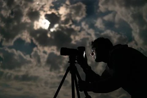 Man shooting the night cloudy sky under moon with a tripod Stock Photos
