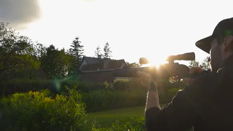 Man shooting a rifle with a scope in a sunny garden at sunset Stock Footage 343718506