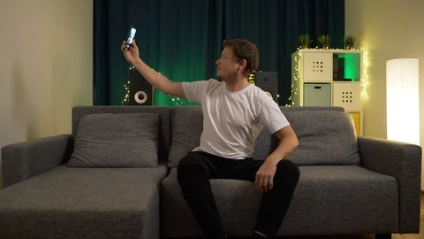 Man shoots himself with a camera phone sitting at home on the sofa Stock Footage 129384440