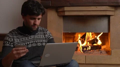 Man shopping online using laptop at home sitting by the fireplace Stock Footage 147193579