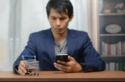 Man Shopping Online Using Smartphone with Small Toy Shopping Cart on Wooden.. Stock Photos
