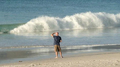 Man at shoreline with breaking waves searching out to sea 動画素材 103482953