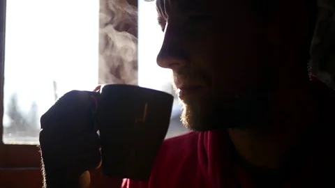 Man with a short beard, sitting naprtiv window with the sun, drinking a hot cup Stock Footage 73008542