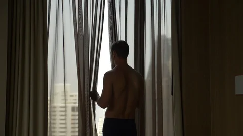 Man in shorts opens the curtains on the window, view from the window Stock Footage 86657084