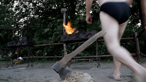 Man in shorts throws firewood in a brazier Stock Footage 100386682