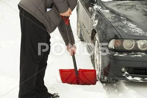 Man with shovel clears snow around the car Stock Photos