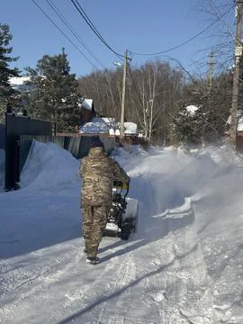 A man shoveling snow while testing a snowblower on a sunny day. Stock Photos